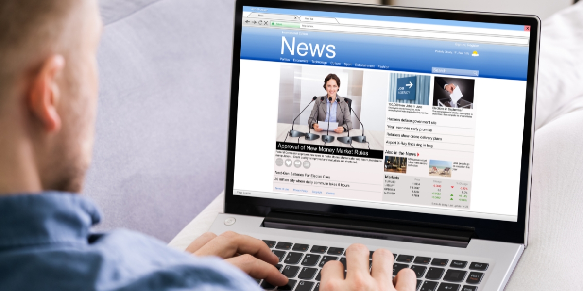 A person views a news website on a laptop displaying financial market data, headlines, and stock information, exemplifying how to navigate authoritative websites for current information and analysis.